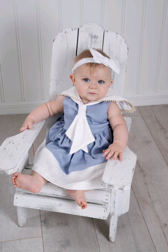 A girl toddler wearing a light blue sailor dress holding a boat