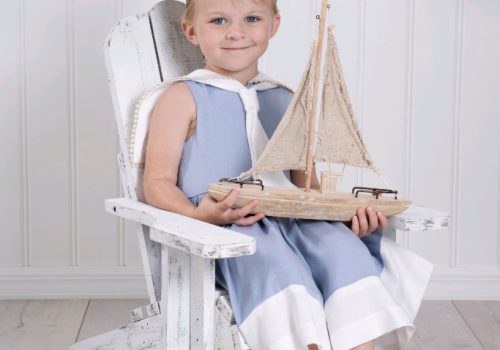 A girl toddler wearing a light blue sailor dress holding a boat