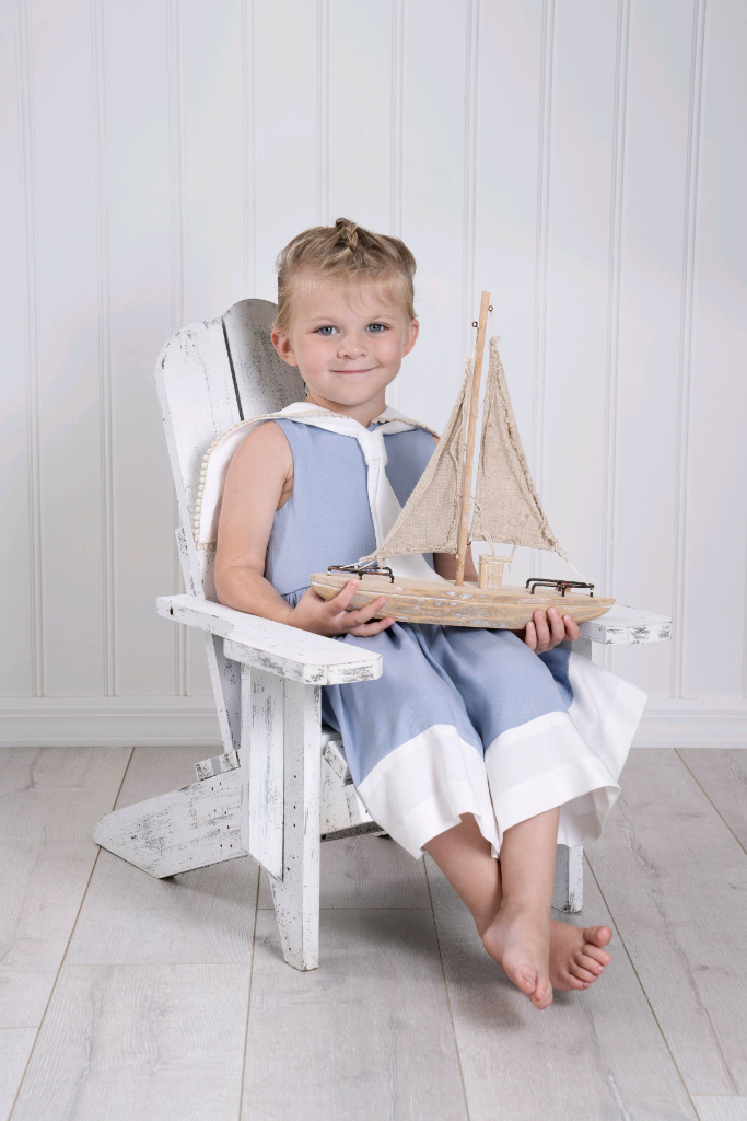 A girl toddler wearing a light blue sailor dress holding a boat